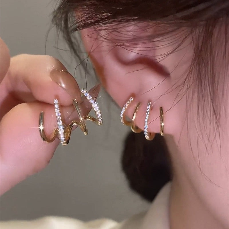 Close-up of a person wearing gold hoop earrings with clear stones.