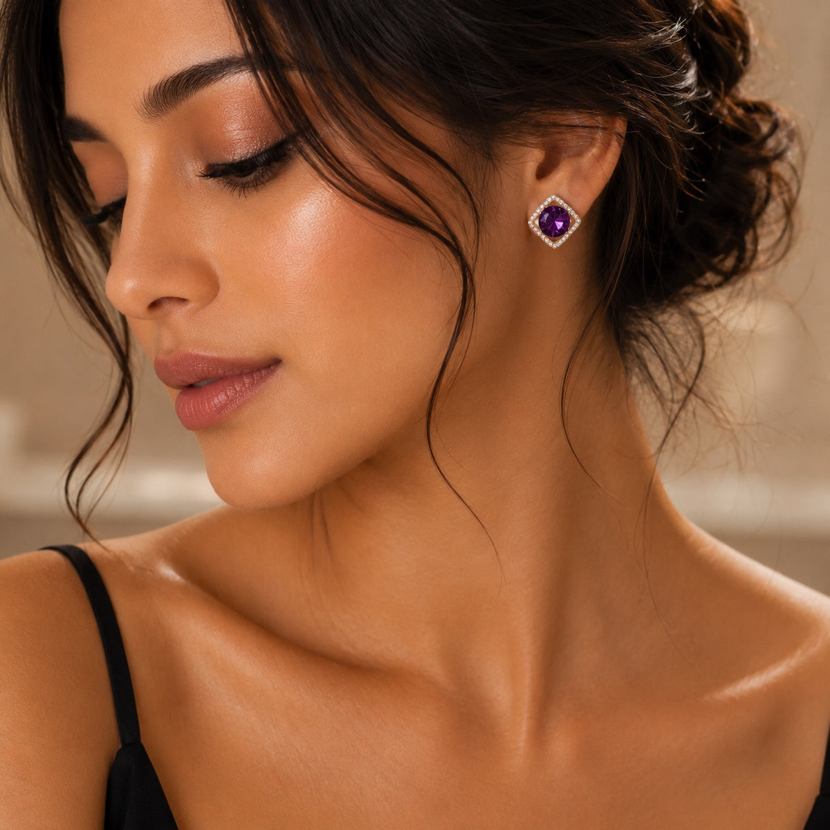 A close-up lifestyle shot of a woman wearing a square stud earring with a deep purple center stone and a halo of small clear stones.