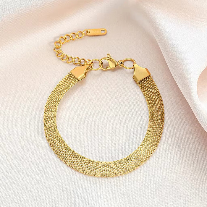 A gold-tone mesh bracelet with a lobster clasp and extension chain, displayed on a soft white fabric background.