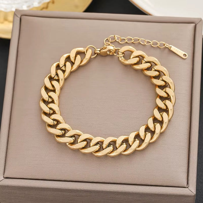 A gold-toned chunky curb chain bracelet displayed on a textured taupe jewelry box.