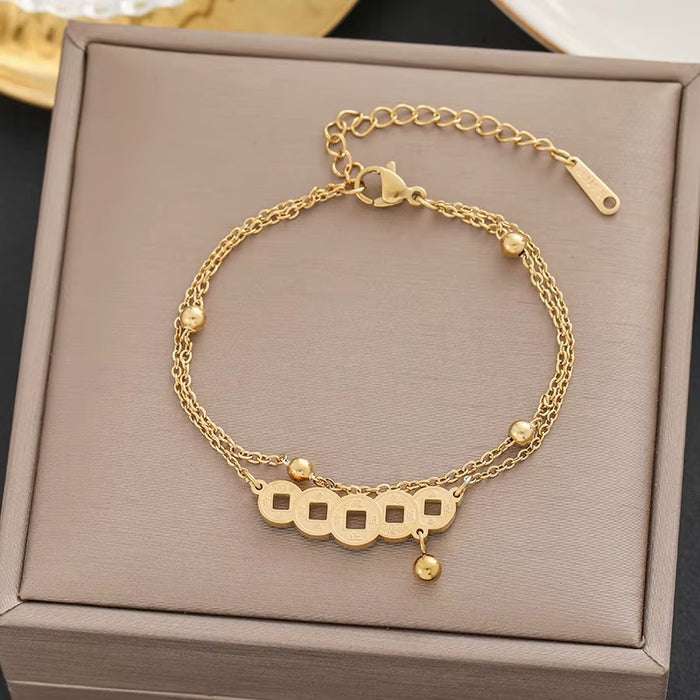 A gold-toned double-strand chain bracelet with five interlocking square coin charms and small bead accents, displayed on a taupe jewelry box.