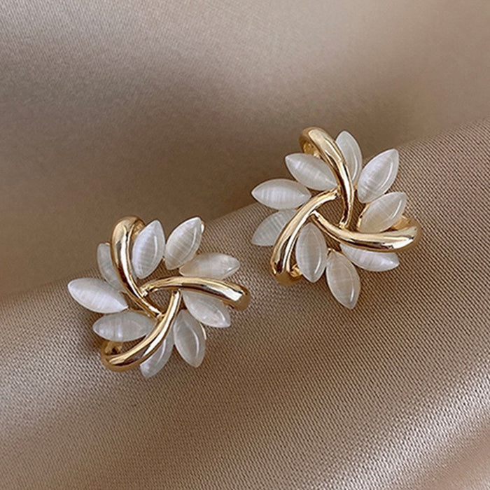 Pair of gold and white earrings on a beige fabric background
