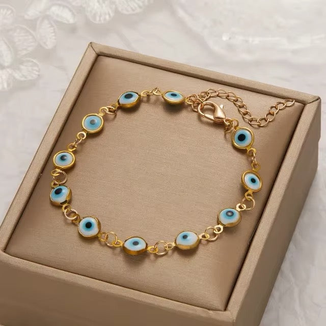 Gold bracelet with blue eye charms on a beige box