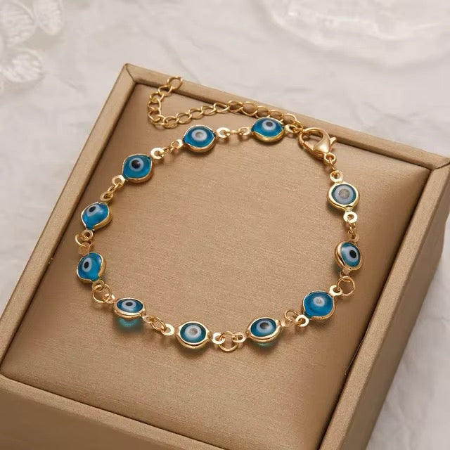 Gold bracelet with blue eye-shaped charms on a beige box