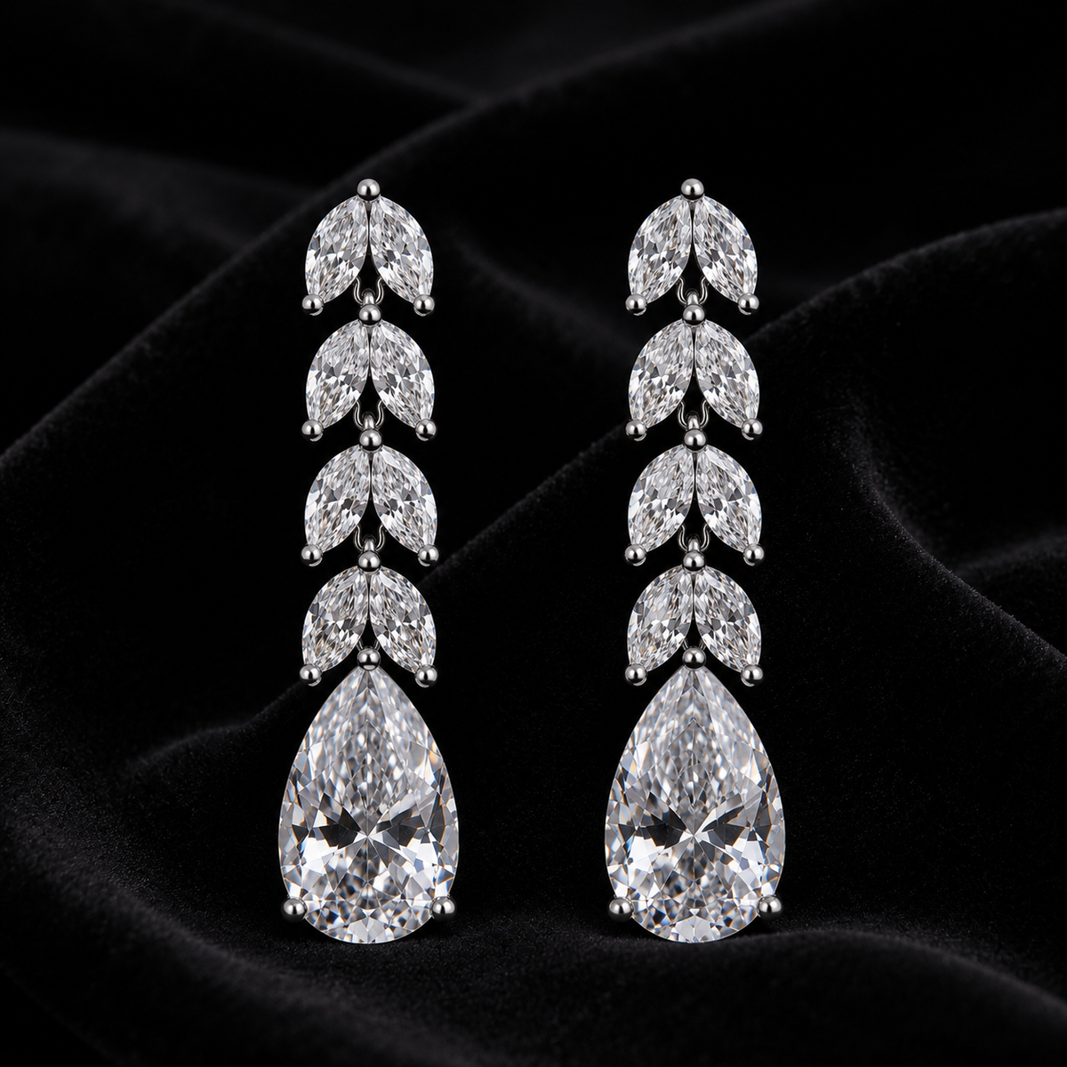 A pair of silver drop earrings with a leaf-like cluster of clear stones above a large pear-cut clear gemstone, displayed on a black velvet fabric background.